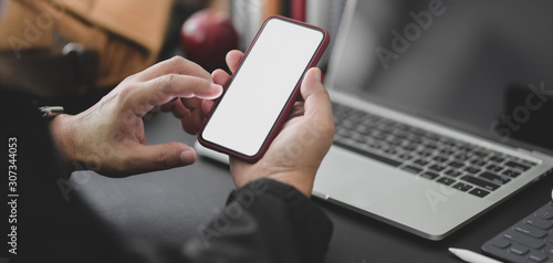 Cropped shot of young professional businessman working on his project while using smartphone in dark modern office