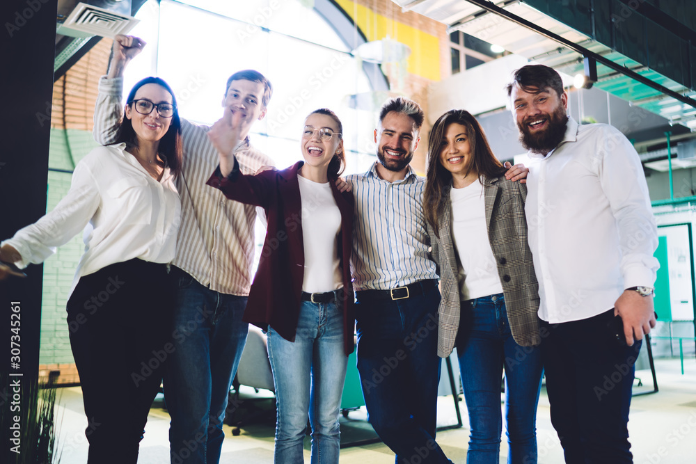 © BullRun - Cheerful work partners standing hugging in workplace