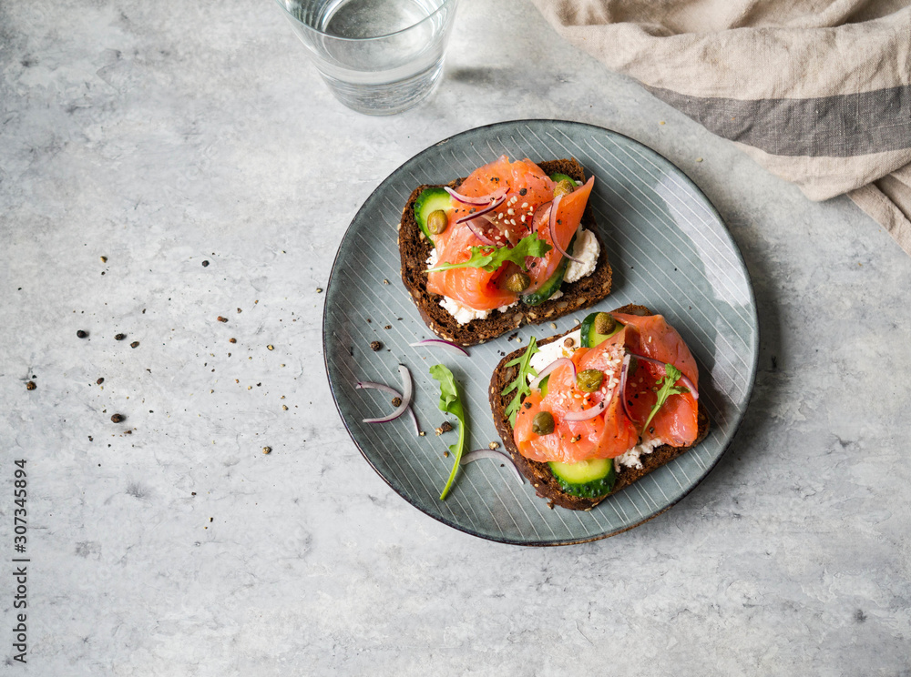 Healthy toasts with rye bread with cream cheese, salmon, fresh cucumber, capers, sesame seeds, black pepper and arugula on plate. Healthy toasts with rye bread with cream cheese, salmon, fresh cucumber, capers, sesame seeds, black pepper and arugula on plate.