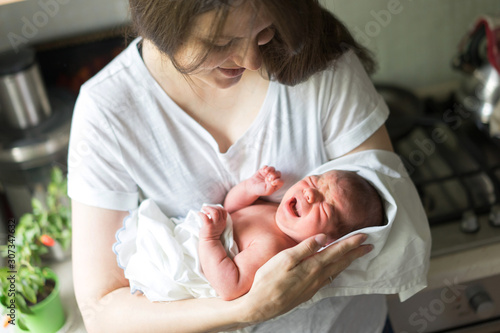 A mother with a newborn baby boy in her arms is breastfeeding him in the kitchen. Colic stomach pain in the abdomen in a newborn baby. Selective focus