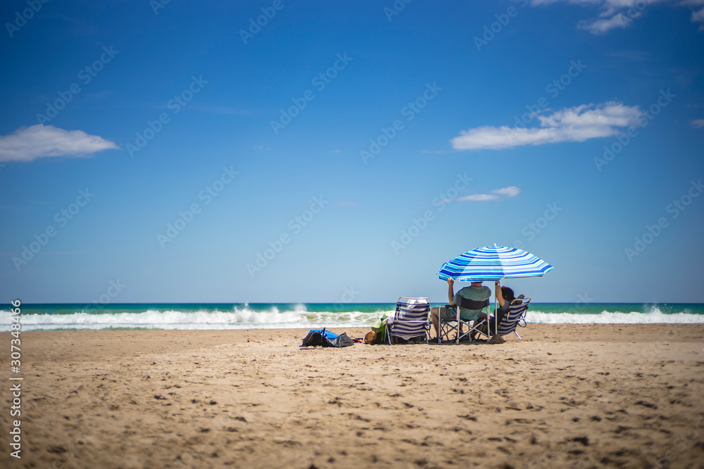 Couple under a umbrella, on a spanish beach, El Campello, Muchavista Playa, Alicante, Spain Couple under a umbrella, on a spanish beach, El Campello, Muchavista Playa, Alicante, Spain