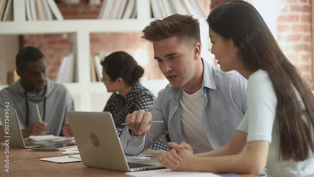 Young guy explaining educational material to interested asian colleague. Young guy explaining educational material to interested asian colleague.