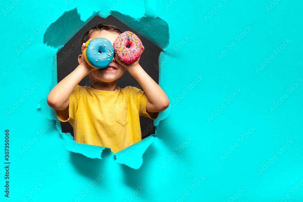 Happy cute boy is having fun played with donuts on black background wall. - obrazy, fototapety, plakaty 