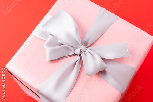 Single pink gift box with silver ribbon on red background.