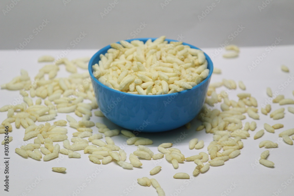 Puffed rice on the blue bowl with white background and some buffed rice are spreading on the floor Puffed rice on the blue bowl with white background and some buffed rice are spreading on the floor