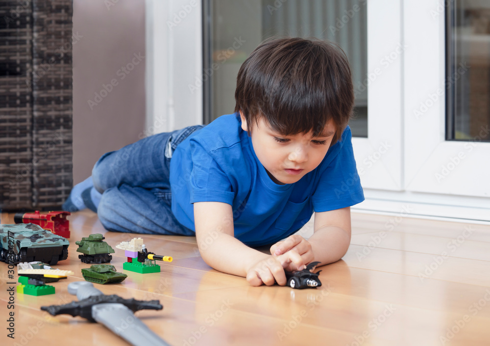 Active boy crawling on floor playing with soldiers and tank toys in playroom, Happy Kid playing wars and peace on his own, Child relaxing at home on weekend, Children imagination and development Active boy crawling on floor playing with soldiers and tank toys in playroom, Happy Kid playing wars and peace on his own, Child relaxing at home on weekend, Children imagination and development