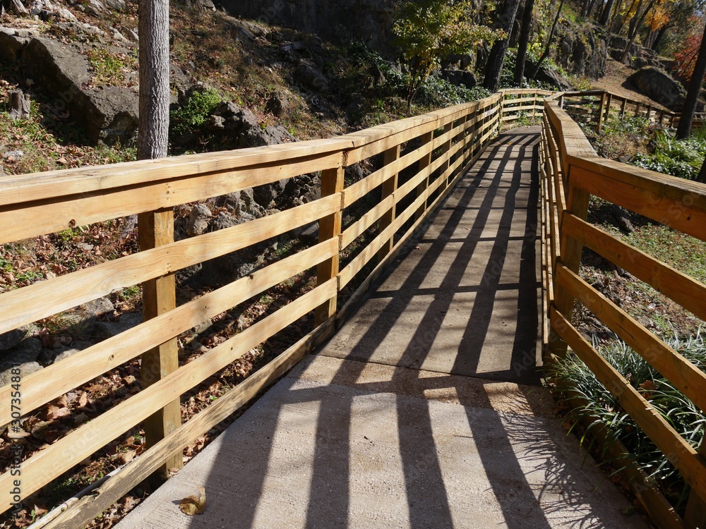 Close up of a  wooden walkway with railings by the side of a flowing spring in autumn