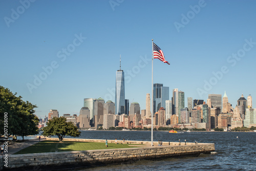 Panorama of New York with Liberty Island in the foreground with a American Flag waving in the wind on a summer day, New York, United States of America.