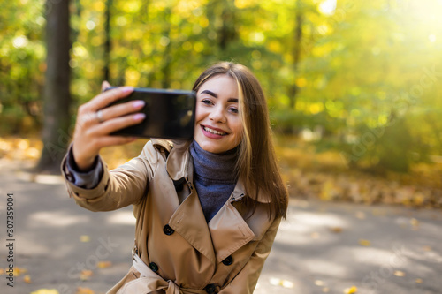 Positive young woman making selfie while drinking coffee in autumn park. © F8  \ Suport Ukraine