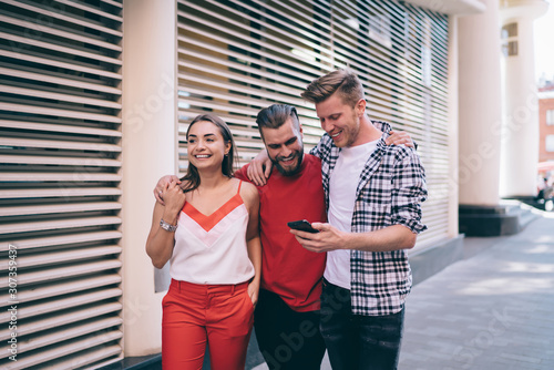 Photography Cheerful relaxed friends using smartphone on street while lounging together in d