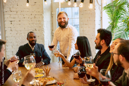 Happy co-workers celebrating while company party  corporate event. Young caucasian people in business attire talking  drinking wine. Concept of office culture  teamwork  friendship  holidays  weekend.