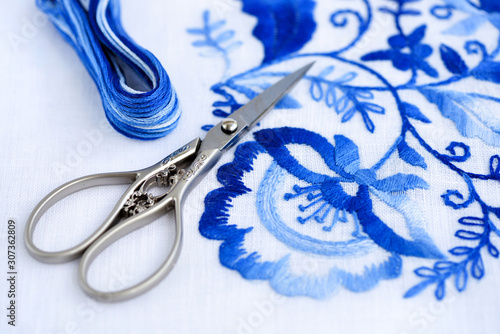 Embroidery, thread and scissors. Blue floral ornament on a white background. Art and craft conception.