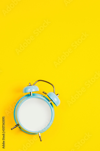 Vintage blue blank alarm clock on a yellow background with marskmallows as a decoratio