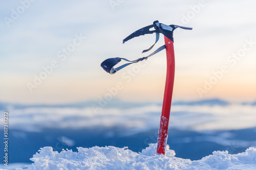 Expedition equipment for winter climbing - ice-axe in natural conditions at stunning sunset scene in mountains background. photo