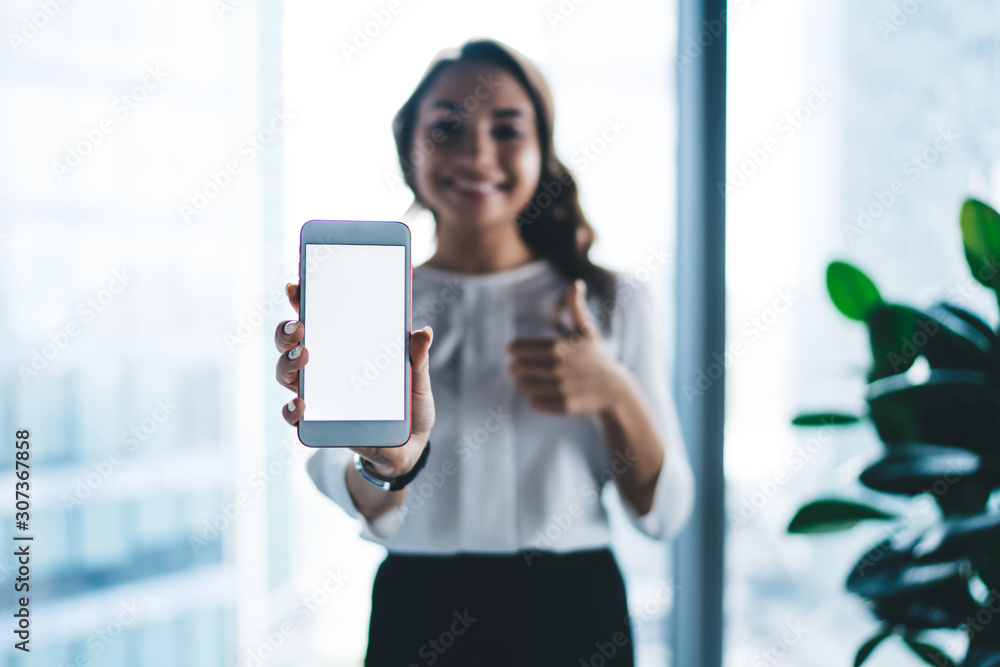 Pretty smiling female office worker showing smartphone in office Pretty smiling female office worker showing smartphone in office
