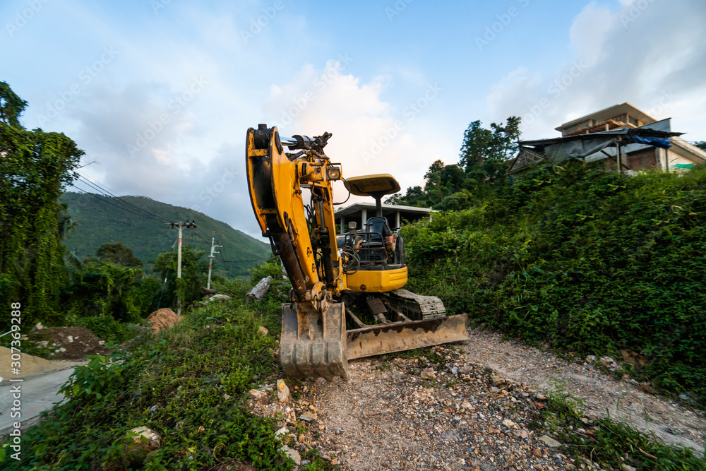 The modern excavator on the construction site with sunset sky. Large tracked excavator standing on a hill with a green grass. Machinery for a construction of a new building in the countryside. The modern excavator on the construction site with sunset sky. Large tracked excavator standing on a hill with a green grass. Machinery for a construction of a new building in the countryside.