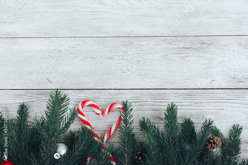 Christmas background concept. Heart shaped candy canes, Christmas baubles, fir tree branches, candy cane, cones on white wooden table. New Year, winter holiday, copy space, top view