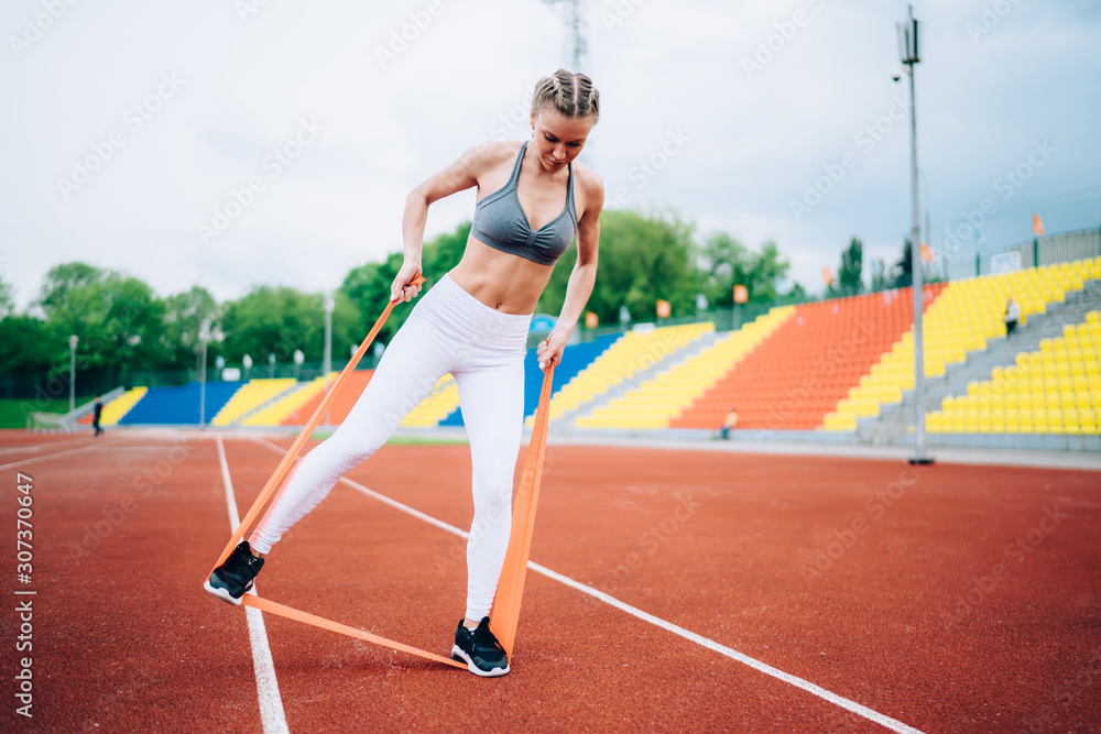 Adult athletic female training with rubber band in stadium