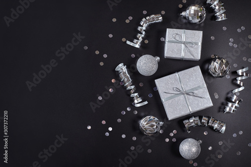 Present boxes, silver christmas balls and ribbons on black background with copy space