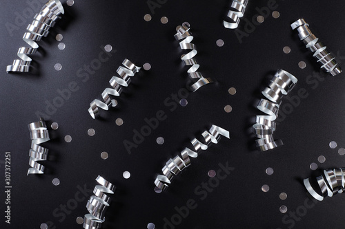 Silver ribbons and confetti on black background.