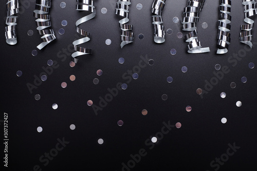 Silver ribbon and confetti on black background. New year backdrop.