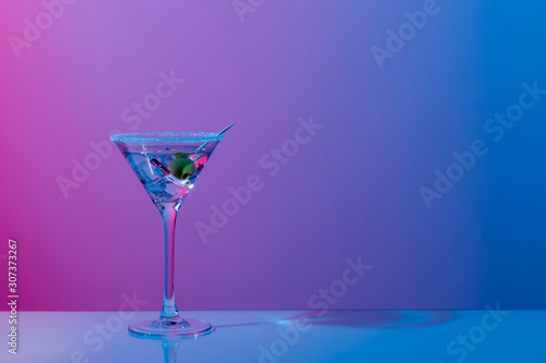 Martini cocktail with ice cubes, olive, sugar rim in neon pink and blue light on mirror bar. Night club, party, cocktail menu concept. Close-up, copy space