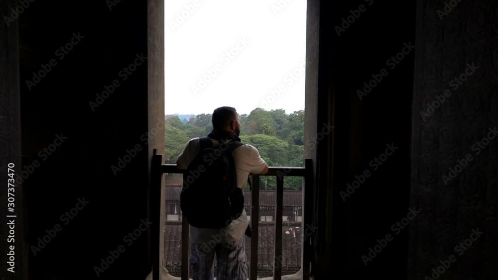 Man looking at ancient Angkor Wat complex temple ruins in Cambodia Man looking at ancient Angkor Wat complex temple ruins in Cambodia