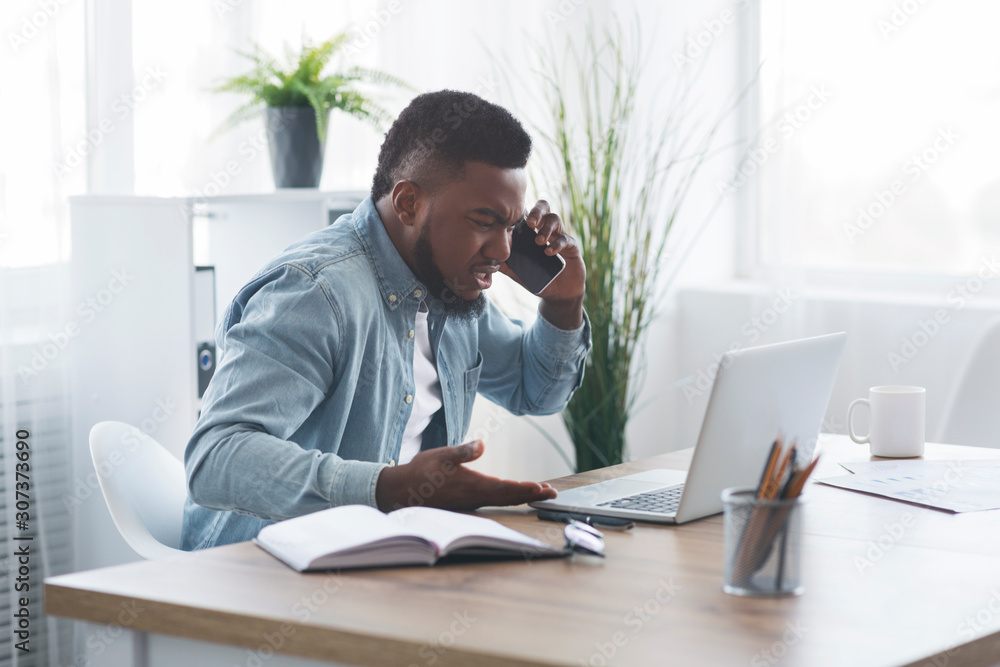 Disappointed businessman talking on phone, and looking at laptop with anger Disappointed businessman talking on phone, and looking at laptop with anger
