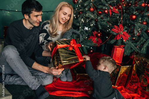 Portrait of Family Mom Dad with One Little Kid Playing in Room Decorated in Christmas Theme photo