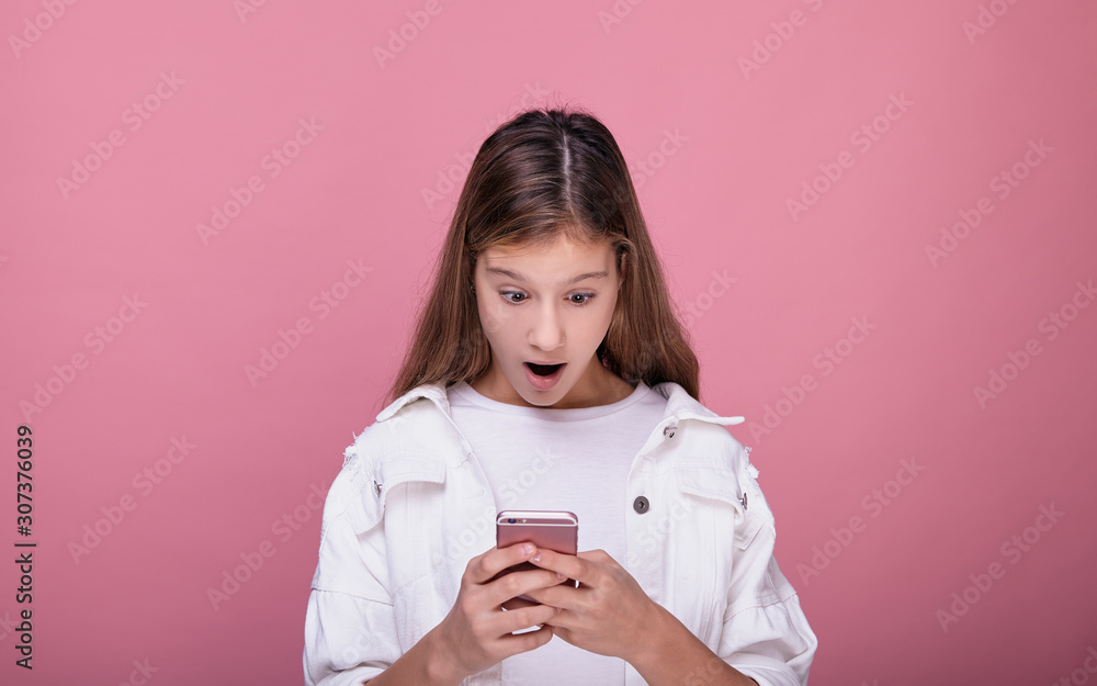 A pretty teenager girl opened her mouth in surprise and looks at the phone. A pretty teenager girl opened her mouth in surprise and looks at the phone.