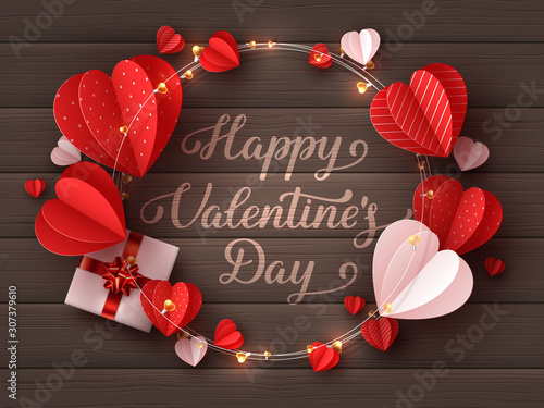 Happy Valentines day greeting card. Decorative paper cut hearts, gift box, garland with handwritten lettering text on brown wooden background. Vector illustration.