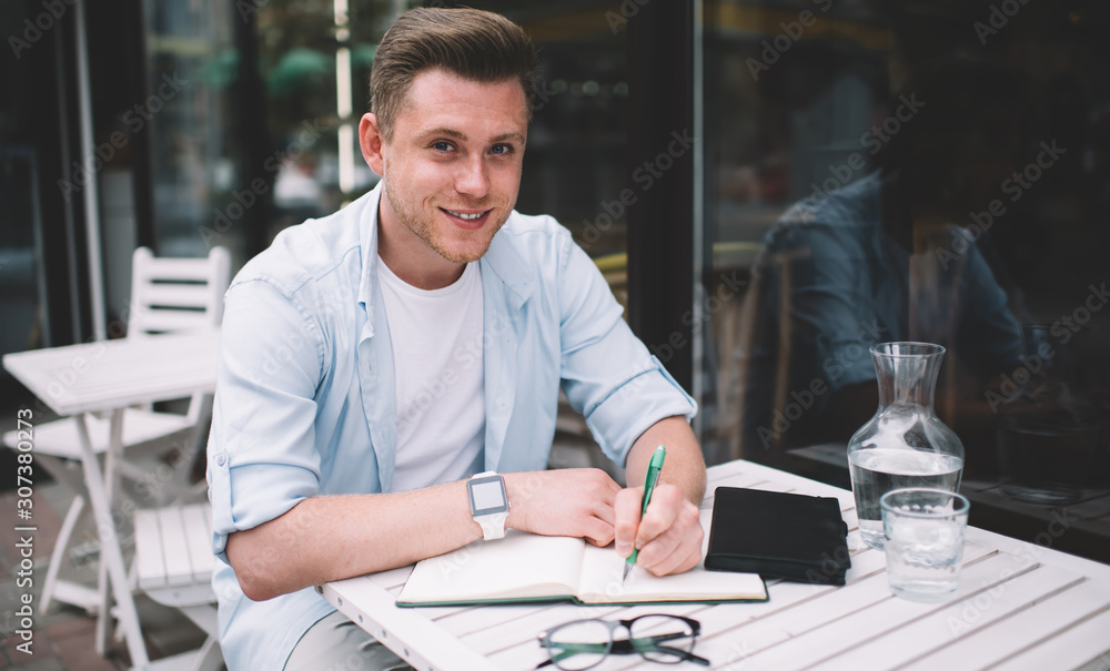 Fototapeta premium Cheerful guy making notes in outdoor terrace