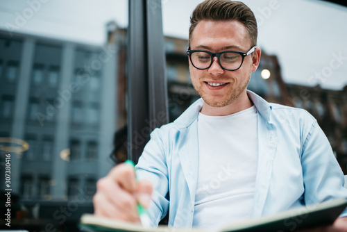 Happy young guy making notes in cafe