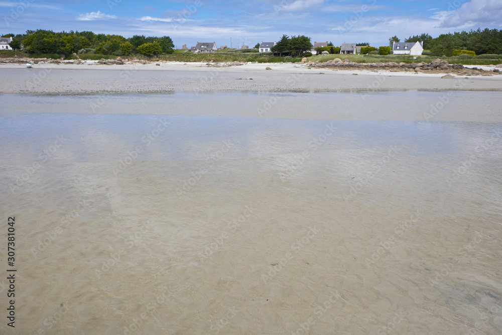 Low tide with shallow water and white sand, view to the coastline with trees and holiday houses, relaxed summer feeling