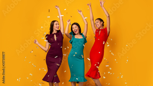Three Happy Girls Dancing Under Falling Confetti Over Yellow Background