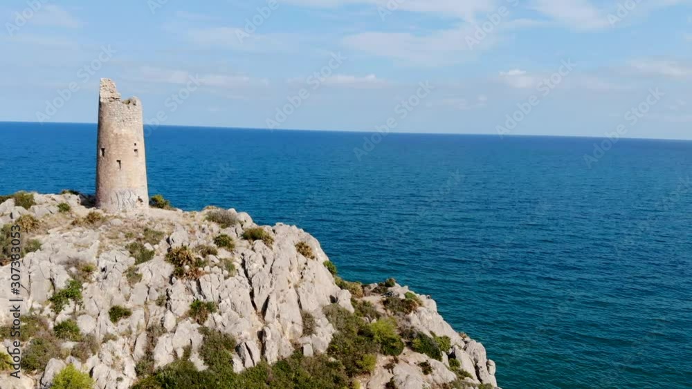 Drone flies over a coastal watchtower, centuries-old tower on cliff the sea and blue sky with rocks in lateral traveling Drone flies over a coastal watchtower, centuries-old tower on cliff the sea and blue sky with rocks in lateral traveling