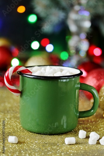 hot cocoa or chocolate with marshmallows and Christmas candy in an enameled mug against the background of festive lights and bokeh. place for text. copy space