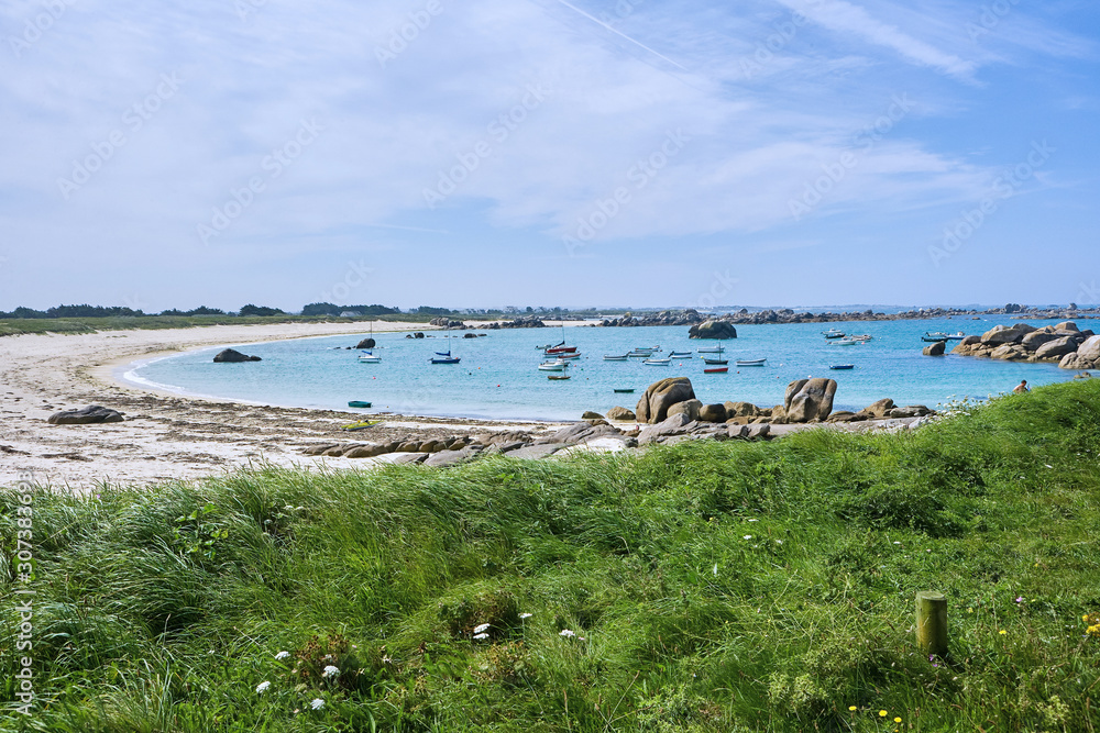 View to an idyllic small bay with grass, sand and little rocks, small boats in the water, summer holiday feeling