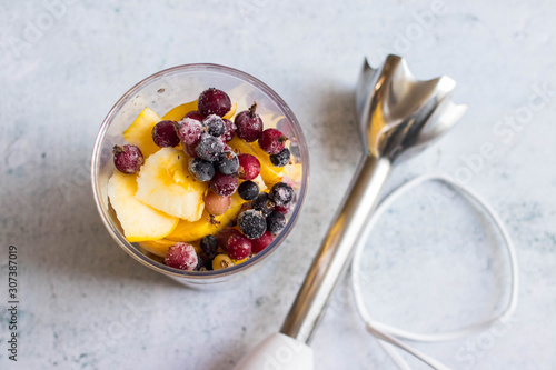 Fototapeta Naklejka Na Ścianę i Meble -  Frozen berries, cut apples, bananas and other fruits in plastic blender glass or flask. Ready to make pulp or smoothie. Vegan or vegetarian food concept. Morning time light.