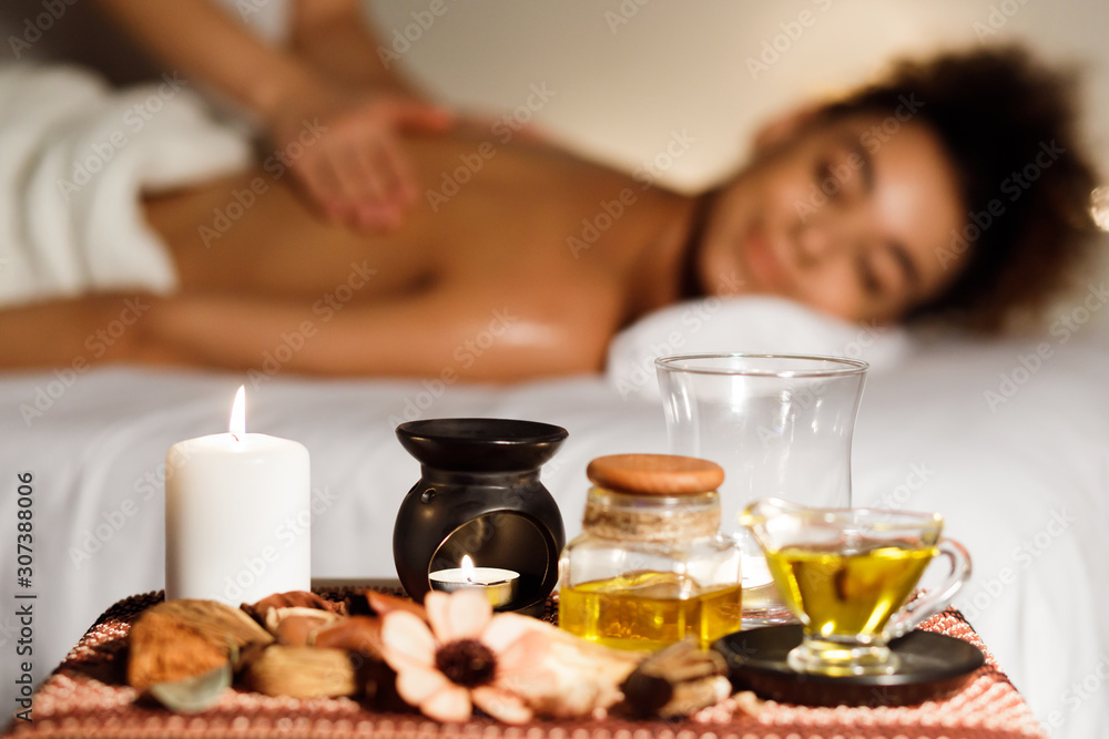 Afro girl enjoying back massage with aroma candle and oils