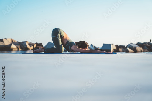 Slim woman doing yoga in Half Tortoise position near sea