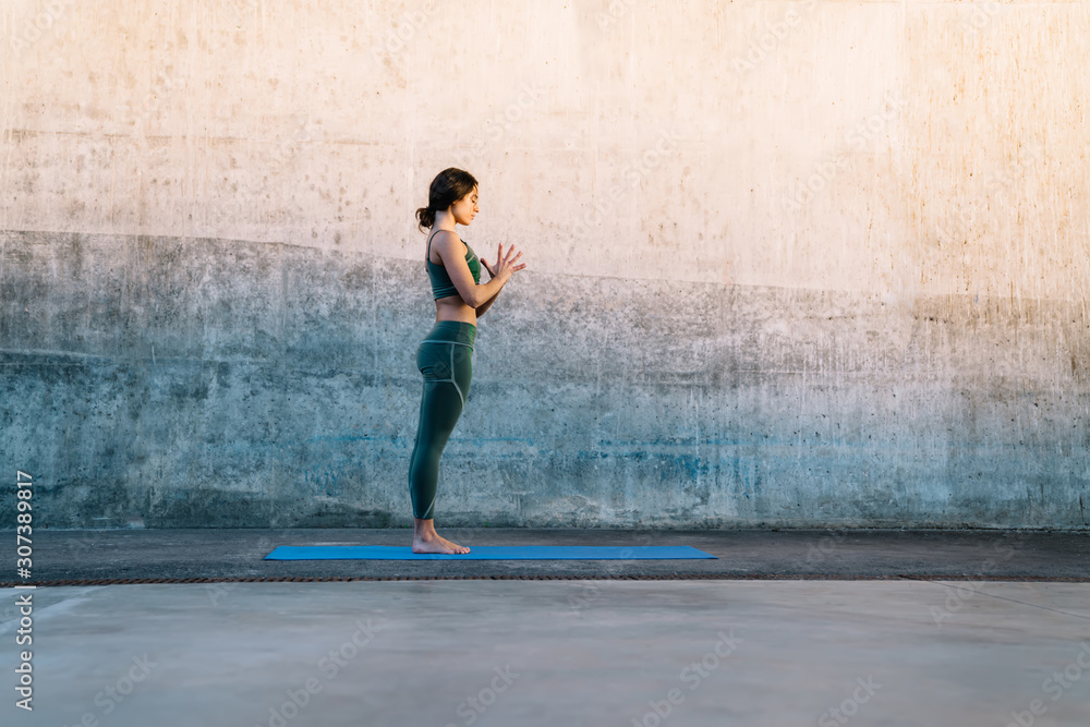 Young serene brunette making Prayer hands yoga pose on fitness mat against concrete wall Young serene brunette making Prayer hands yoga pose on fitness mat against concrete wall