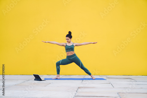 Young sporty slim woman exercising yoga in Virabhadrasana II pose using tablet in yard © BullRun