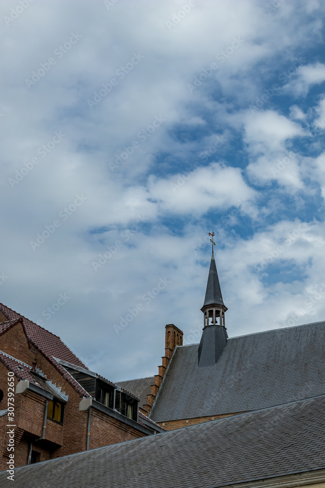 Church roof, tower with cross and dramatic sky. Street view of beautiful historic city center architecture of Bruges or Brugge, West Flanders province, Belgium. Lovely summer August weather