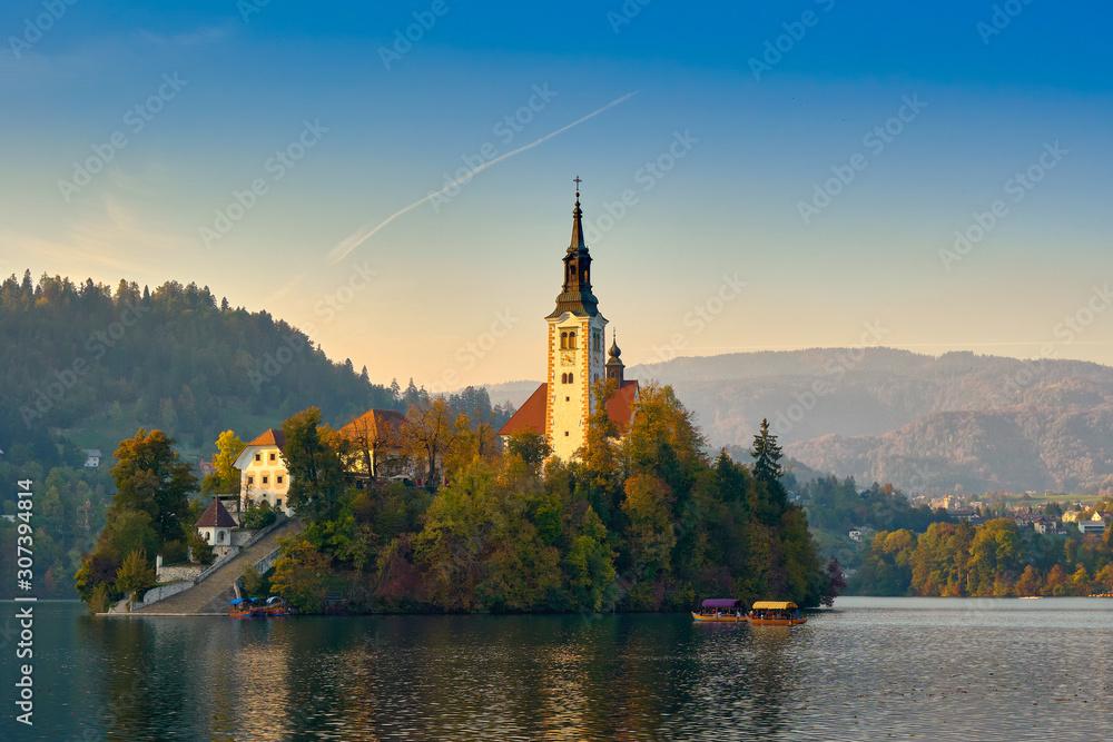 Beautiful church in middle of slovenian Bled lake surrounded by mountains on evening day with blue skies in Bled, Slovenia. Travel landmarks and landscapes concept Beautiful church in middle of slovenian Bled lake surrounded by mountains on evening day with blue skies in Bled, Slovenia. Travel landmarks and landscapes concept