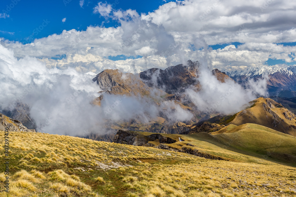 Panoramic mountain view. Beautiful panorama of the Caucasus Mountains with rocky ledges, snowy peaks, yellow meadows, dramatic cloudy sky