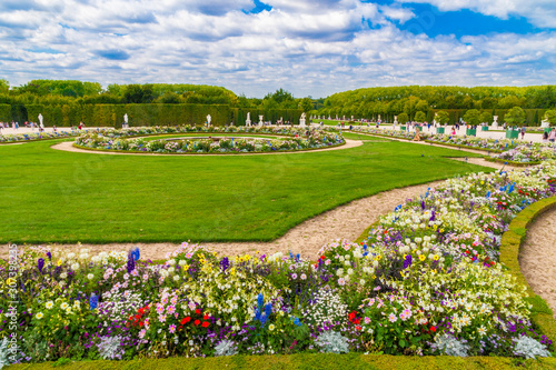 Lovely view of the Latona Parterre in the famous Gardens of Versailles on a summer day. The depicted manicured lawn, flowers, sculptures and a fountain are typical for a classic French formal garden.