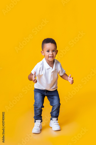 Adorable afro toddler boy showing thumb up gesture over yellow background