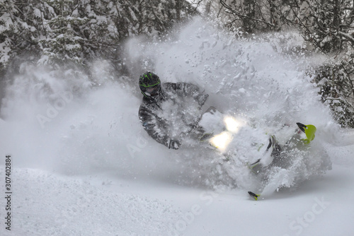 snowmobile rider makes a turn and jump during a snowfall. in the winter forest, leaving behind a trail of big splashes of white snow from a snow bike. bright snowmobile and black suit. snowmobilers photo