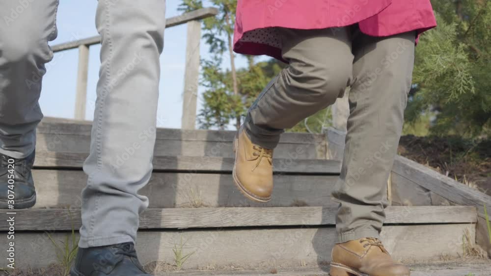 Camera following man's and woman's legs walking down the stairs outdoors. Young couple strolling in autumn park. Dating, romance, togetherness, bonding. Camera following man's and woman's legs walking down the stairs outdoors. Young couple strolling in autumn park. Dating, romance, togetherness, bonding.